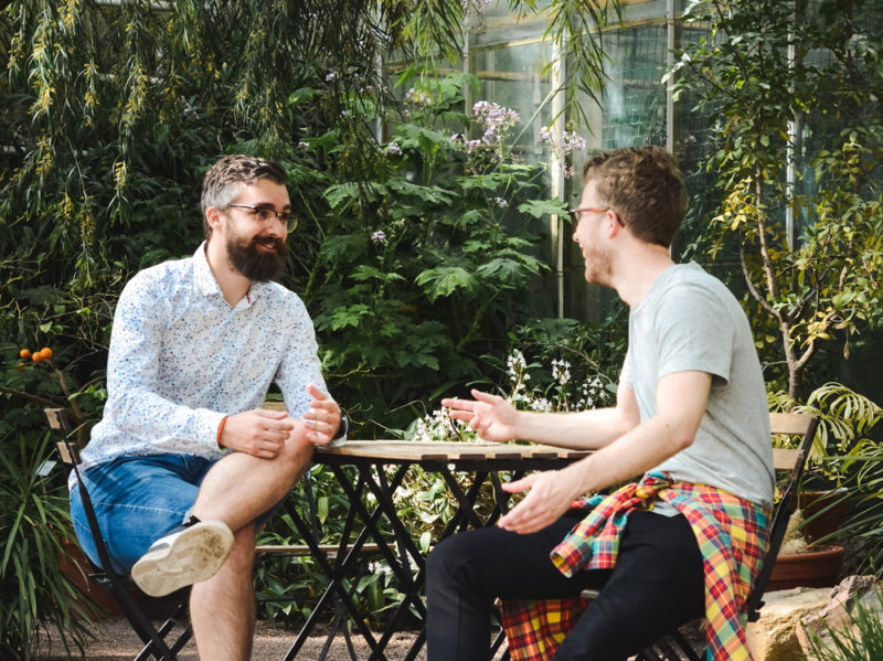 two men talking at table outside