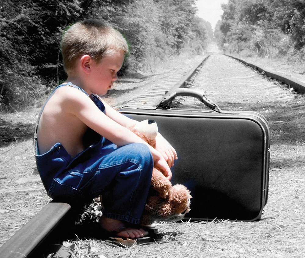 sad boy on railway tracks in overalls with teddy bear and suitcase