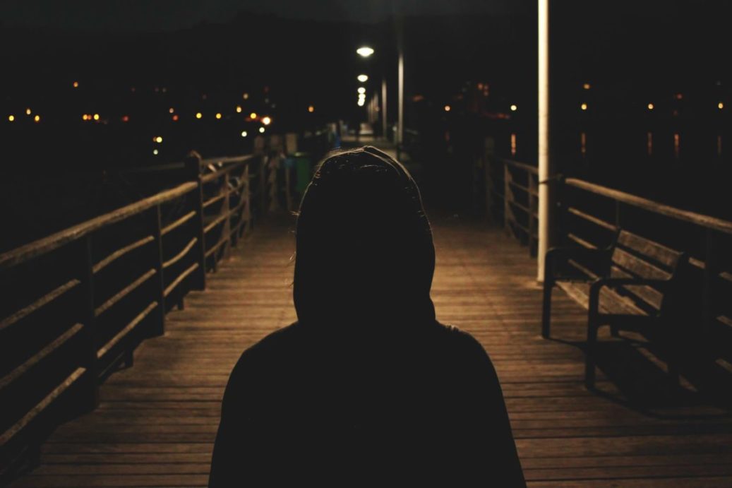 person wearing a hoodie looking at a boardwalk at night