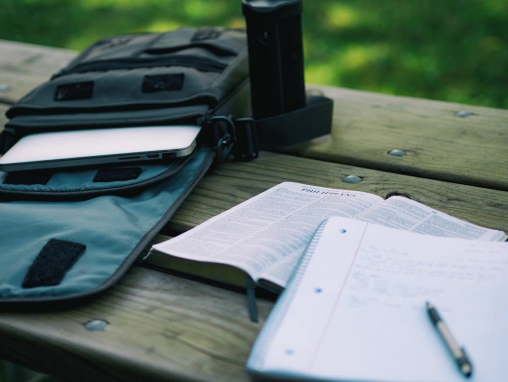 laptop in back pack and book with notebook open on picnic bench