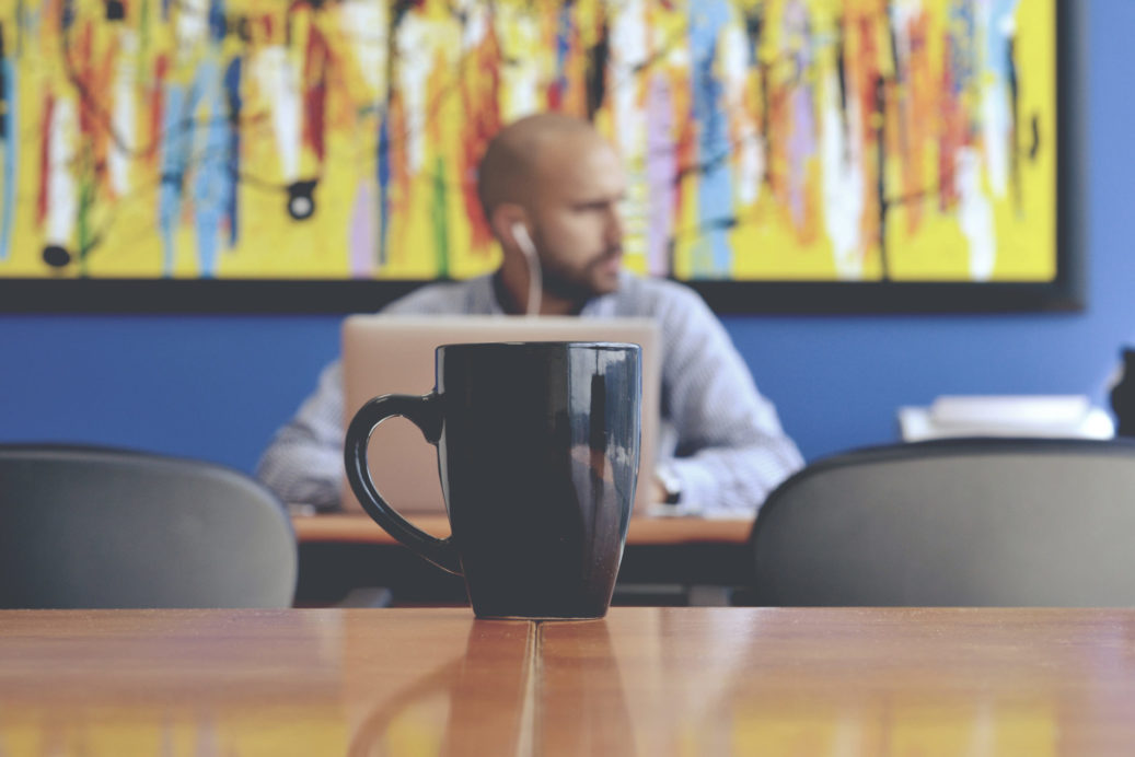 man on laptop with mug in foreground