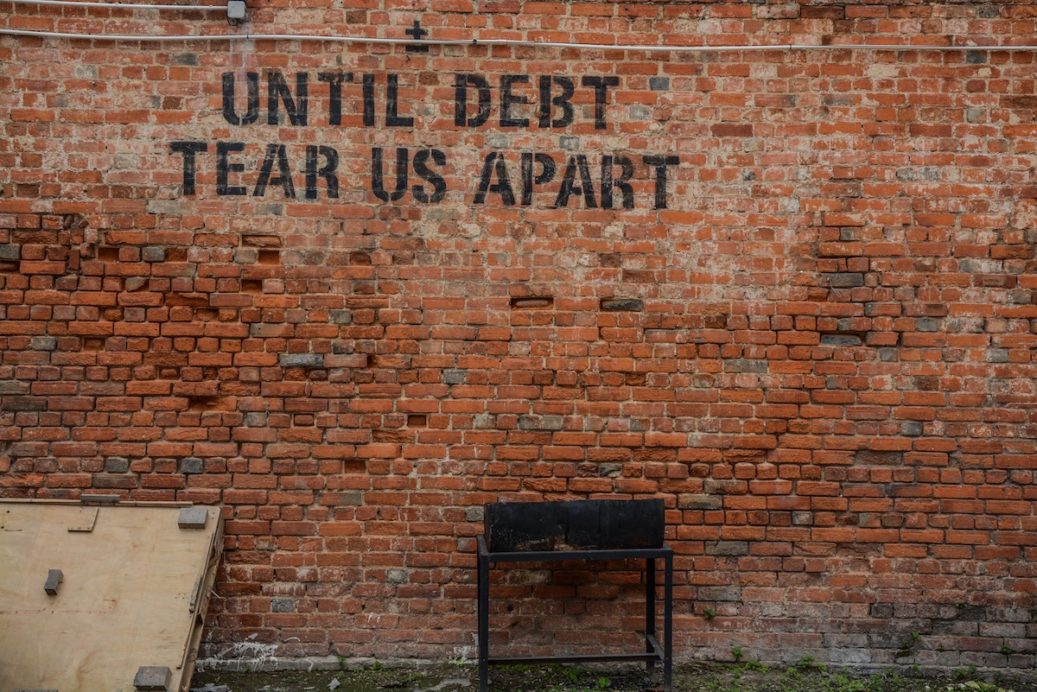 "until debt tear us apart" writing on brick wall