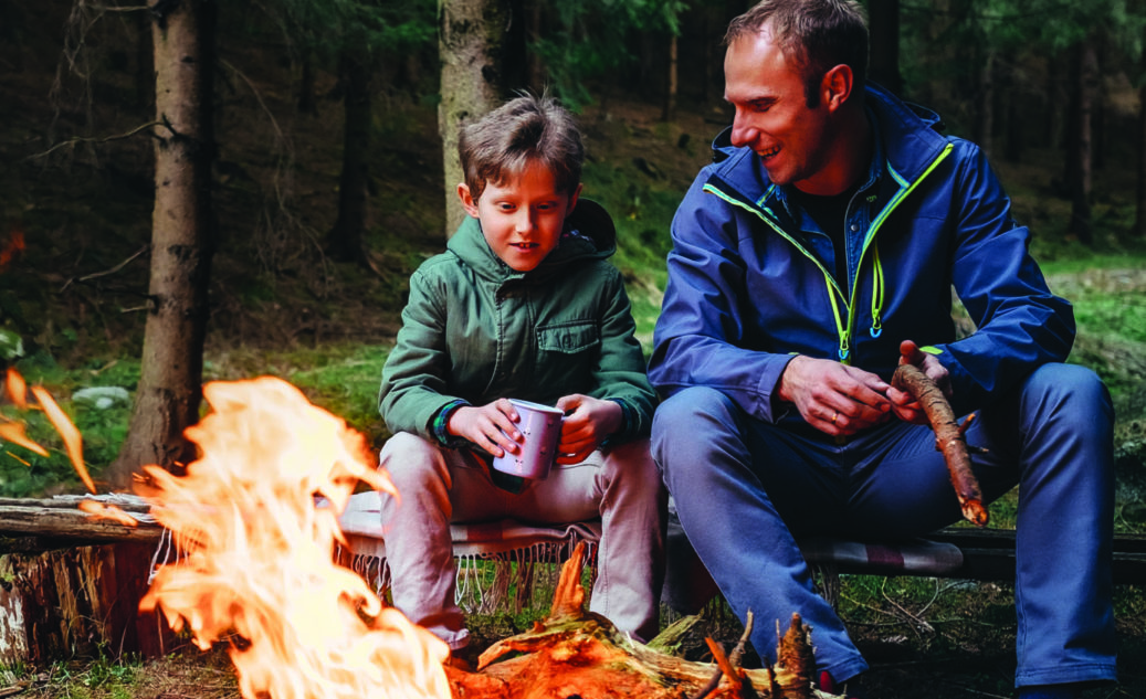 Father with son warm near campfire, drink tea and have conversation