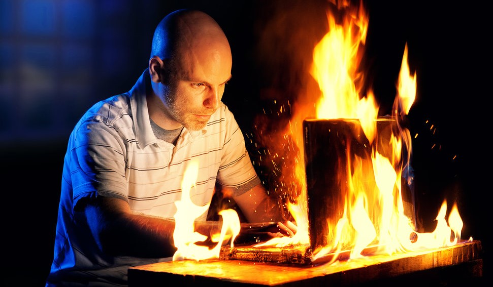 A man uses a laptop while it is engulfed in flames.