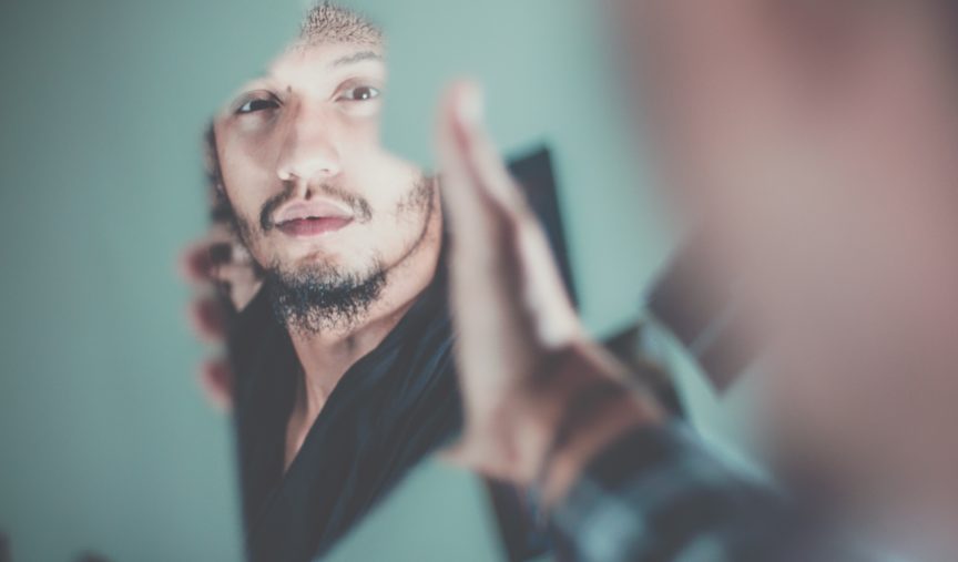 man holding broken mirror looking at himself