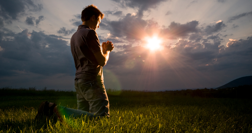 man on knees praying with sun in background