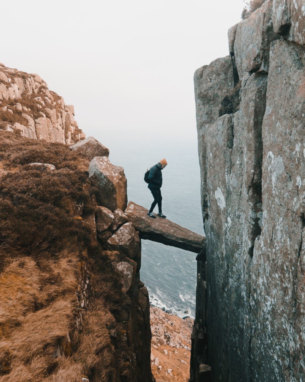 man walking on a big stone in between two cliffs