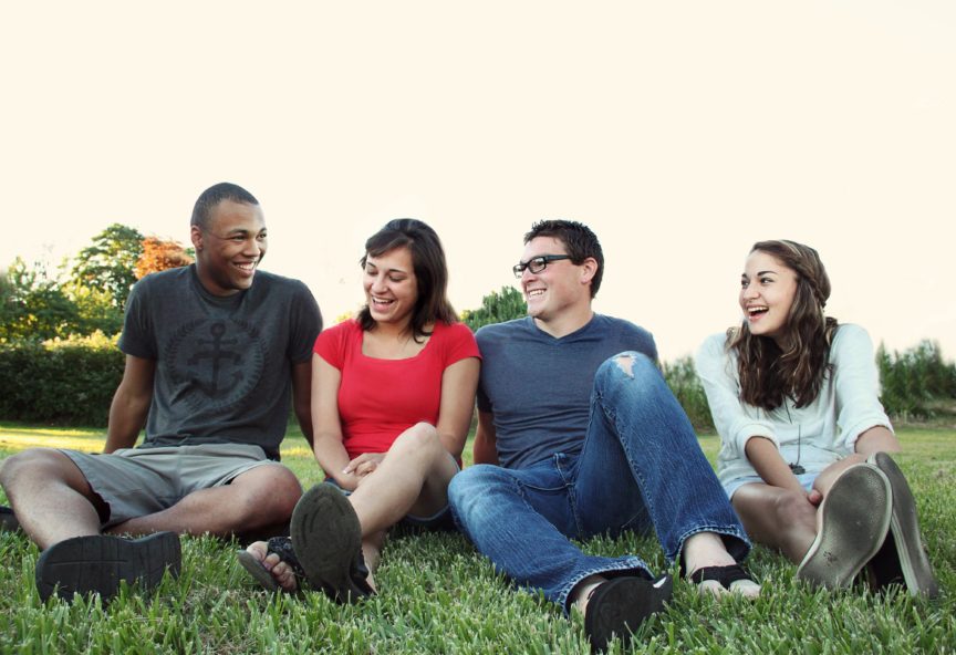 four friends laughing sitting on grass