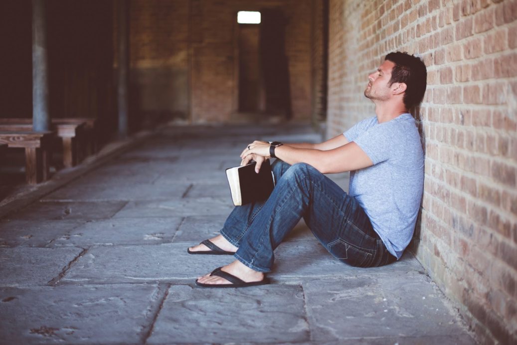 man sitting against wall thinking with Bible
