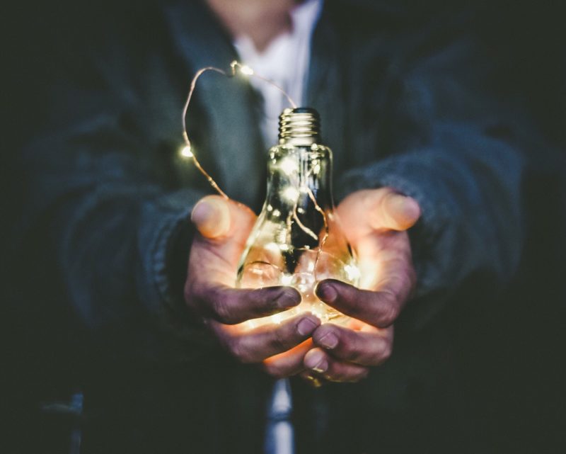 cupped hands holding a lit light bulb