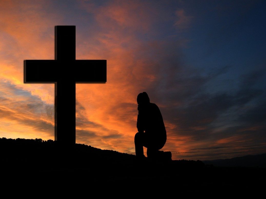 man kneeling at cross sunrise