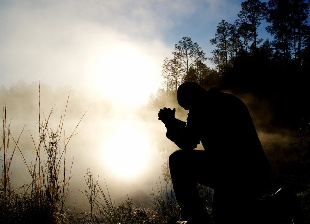 man praying at dawn by the water