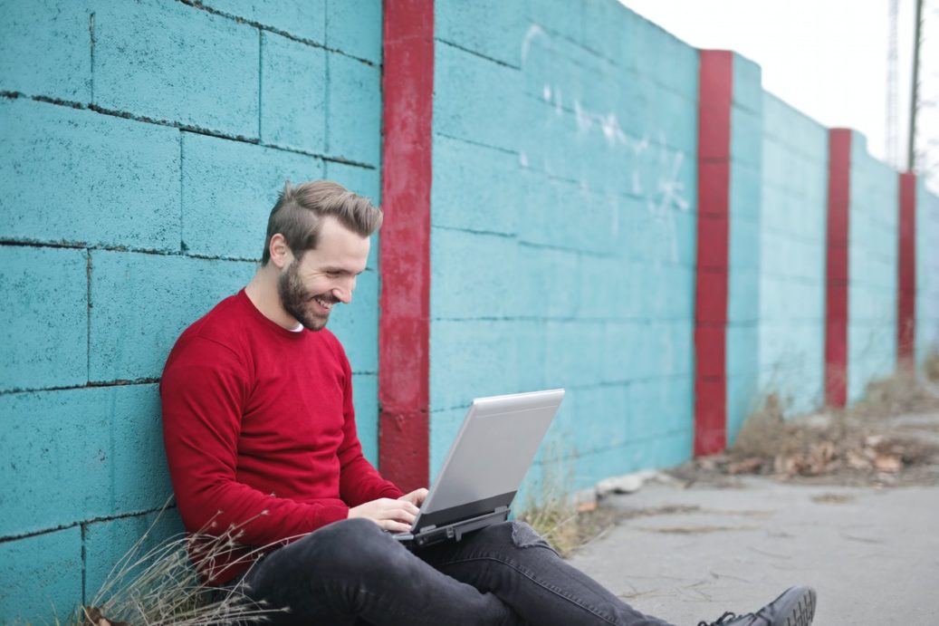 man-leaning-against-wall-using-laptop