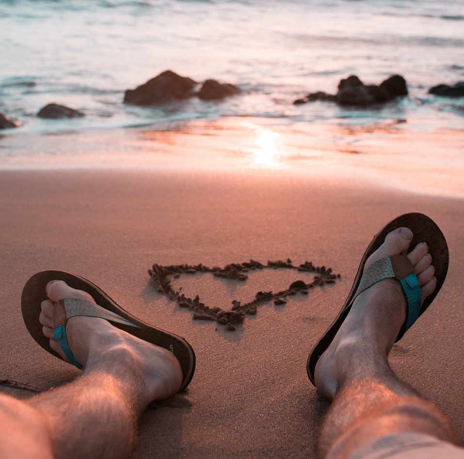 man's feet on beach with heart in the sand